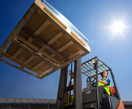 A wide low angle shot of a worker in safety vest using forklift to move the merchandise on a sunny day with a lens flare